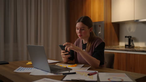 mujer pagando facturas en línea con teléfono móvil en casa. mujer caucásica con suéter beige y usando teléfono inteligente o celular. tocando desplazamiento viendo contenido de video blogs.
