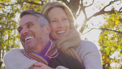 man giving woman piggyback as loving mature couple walk through autumn countryside - shot in slow motion