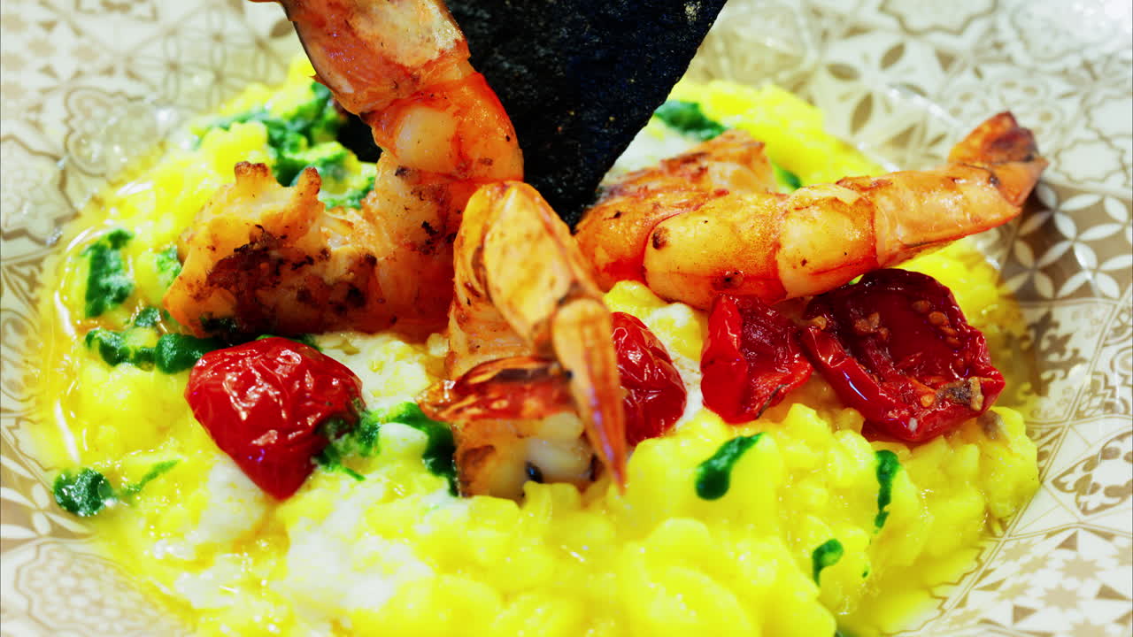 Close up of saffron risotto topped with grilled prawns and roasted cherry tomatoes