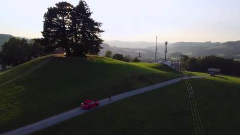 a red ford focus rs drives slowly behind a bicycle driver in a beautiful swiss scenery while sunset