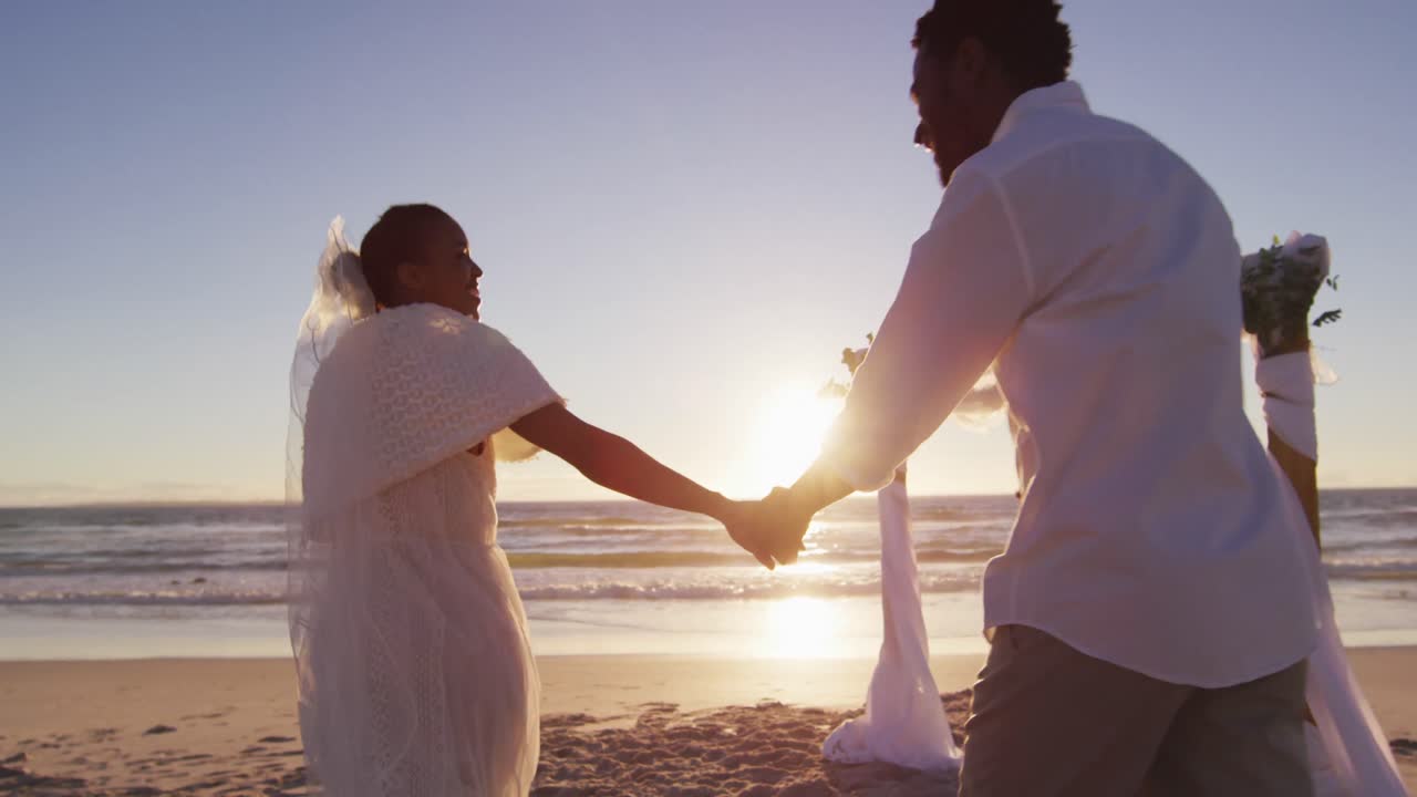 African american couple in love getting married, holding hands on the beach at sunset