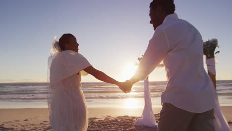 una pareja afroamericana enamorada se casa, tomados de la mano en la playa al atardecer.