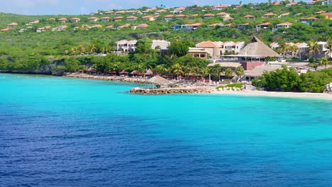 Stunning-blue-Caribbean-waters-with-cabanna-villas-on-coast-of-tropical-island