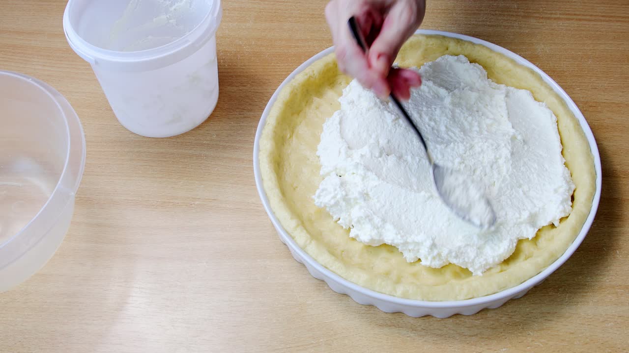 Female hands put cottage cheese on raw dough for homemade cake on kitchen table