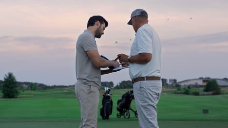 golfing players make deal on green course field. men sign document paper outside