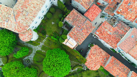 aerial top down shot of gourdon village with colorful rooftops in france surrounded by green forest trees - prores drone shot