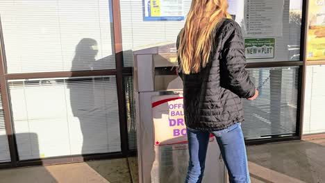 young woman votes in election by mail at official ballot drop box sign for american democratic government presidential race by casting ballot in slot, mail-in letter