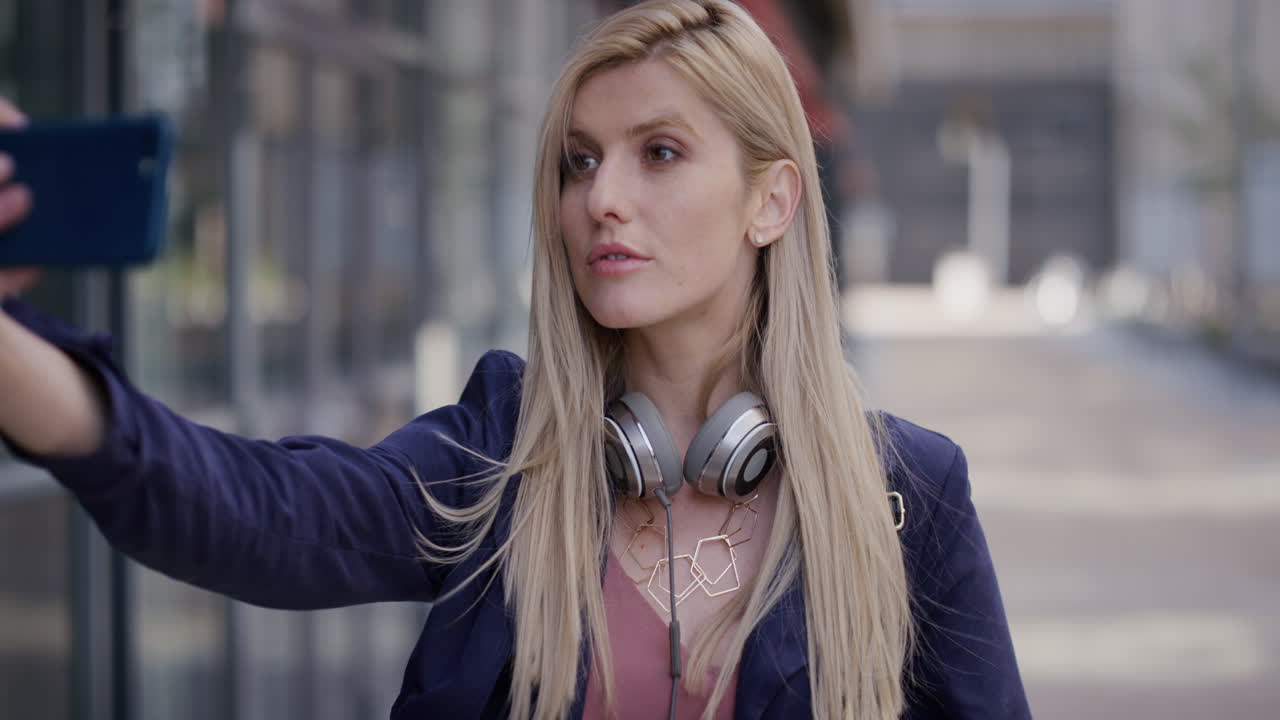 retrato joven hermosa mujer de negocios rubia usando un teléfono inteligente tomando fotos selfie en la ciudad disfrutando posando haciendo caras compartiendo estilo de vida urbano realxed cámara lenta