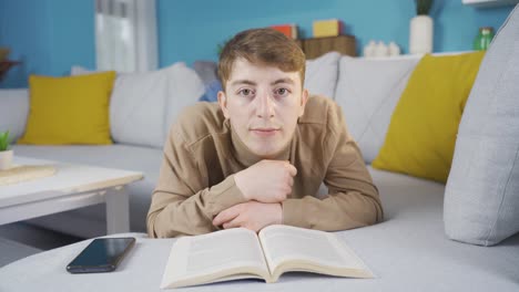 joven mirando aburrido a la cámara mientras lee un libro.