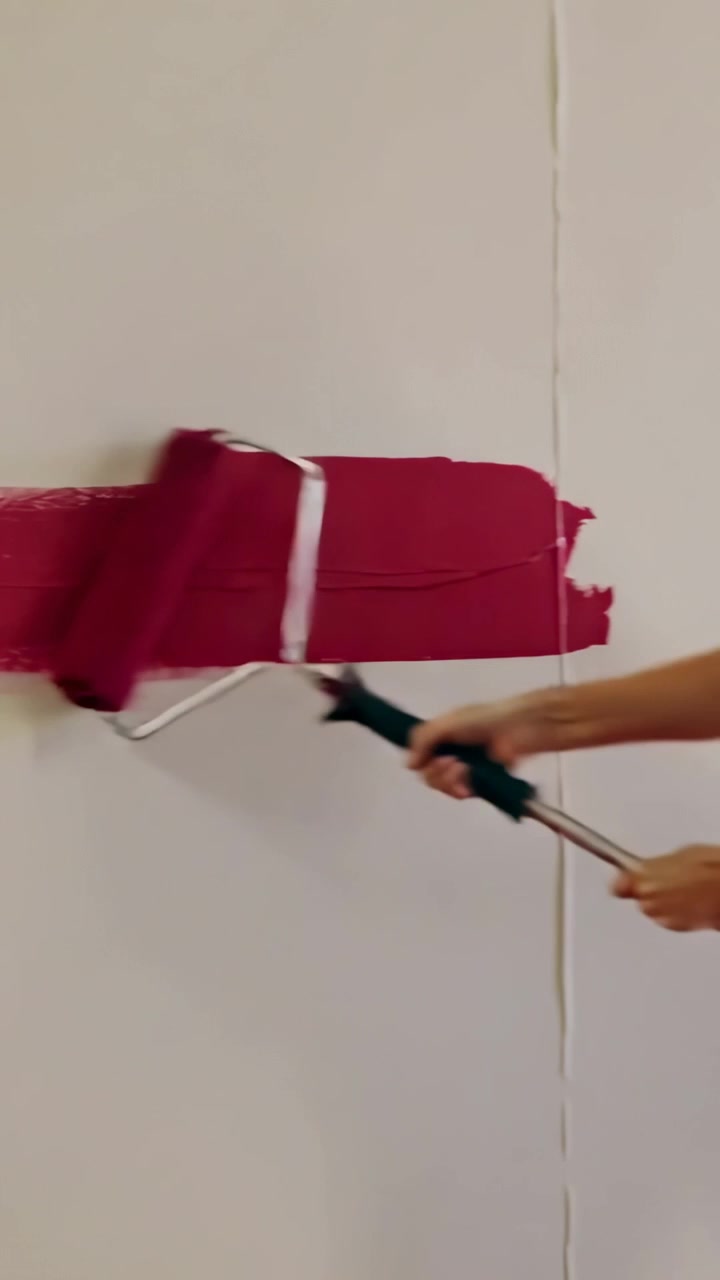 Video vertical: Mano pintando dando la primera pincelada en la pared de una habitación, formando una franja magenta con un rodillo.