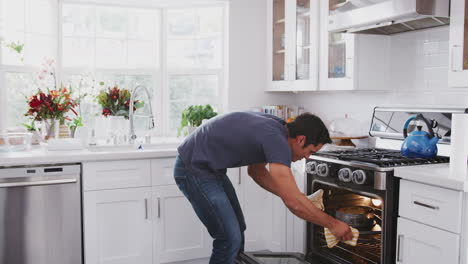 Smiling-millennial-Hispanic-man-takes-a-cake-he’s-baked-out-of-the-oven-and-presents-it-to-camera