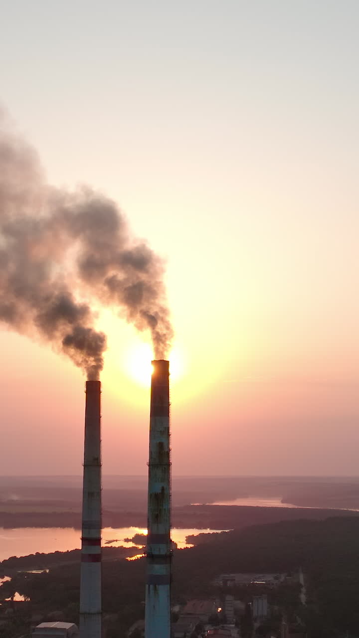 Grandi tubi di fabbrica che fumano al tramonto. Enorme edificio industriale di smog ecologico