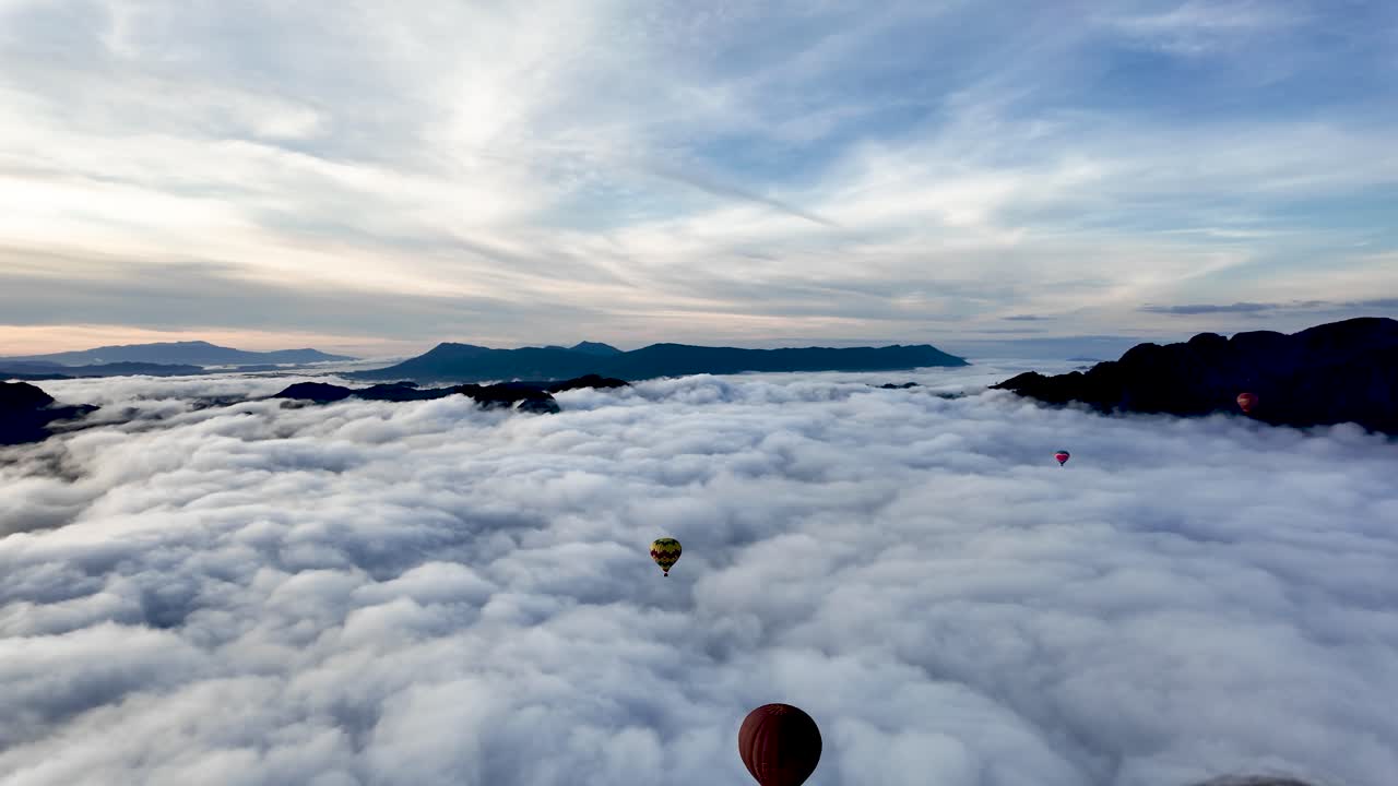 Hot air balloons floating above a sea of clouds and mountain landscape at morning. Pan left shot