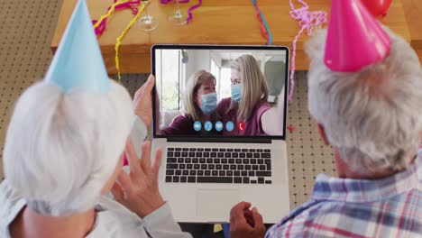 Pareja-Mayor-Caucásica-En-Video-Chat-Portátil-Usando-Sombreros-De-Fiesta-En-Casa