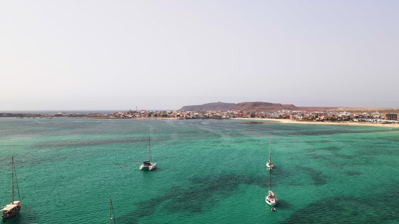 Drone view of the city of Sal Rei, many luxury yachts moored in green ocean, background its old color city and the desert with the mountains
