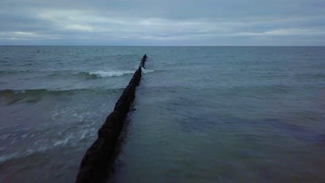 establishing aerial view of baltic sea coast on a overcast day, old wooden pier, white sand beach, low waves crushing against the coast, climate changes, wide angle drone shot moving forward