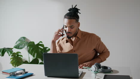 Positive-freelancer-talking-phone-in-light-office-closeup.-Man-working-laptop