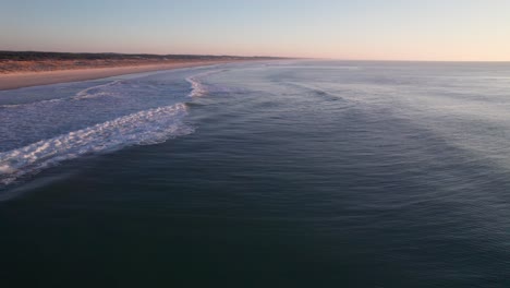 flying over the sea with waves coming onto the beach shore at dusk