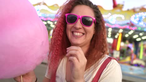 woman with cotton candy lowers her sunglasses and looks at the camera with a smile