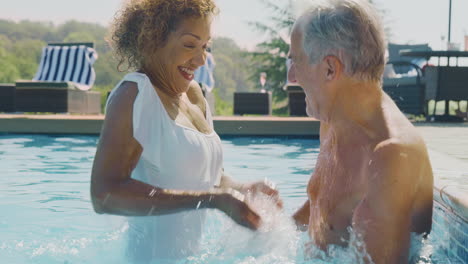 retired senior couple relaxing in swimming pool on summer vacation splashing each other