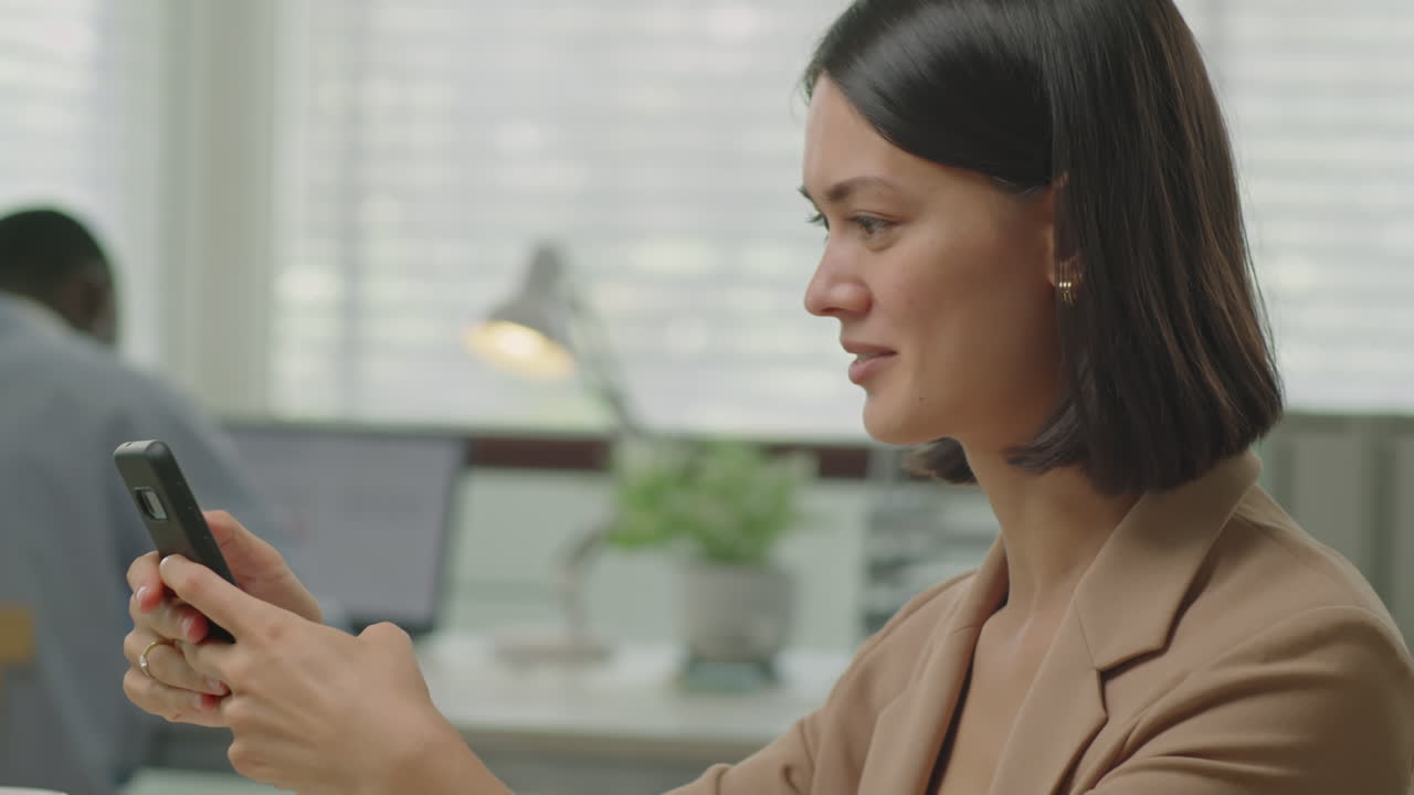 Businesswoman Scrolling on Smartphone at Office Workplace