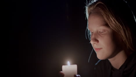 side view: child looking at a candle burning in the dark.