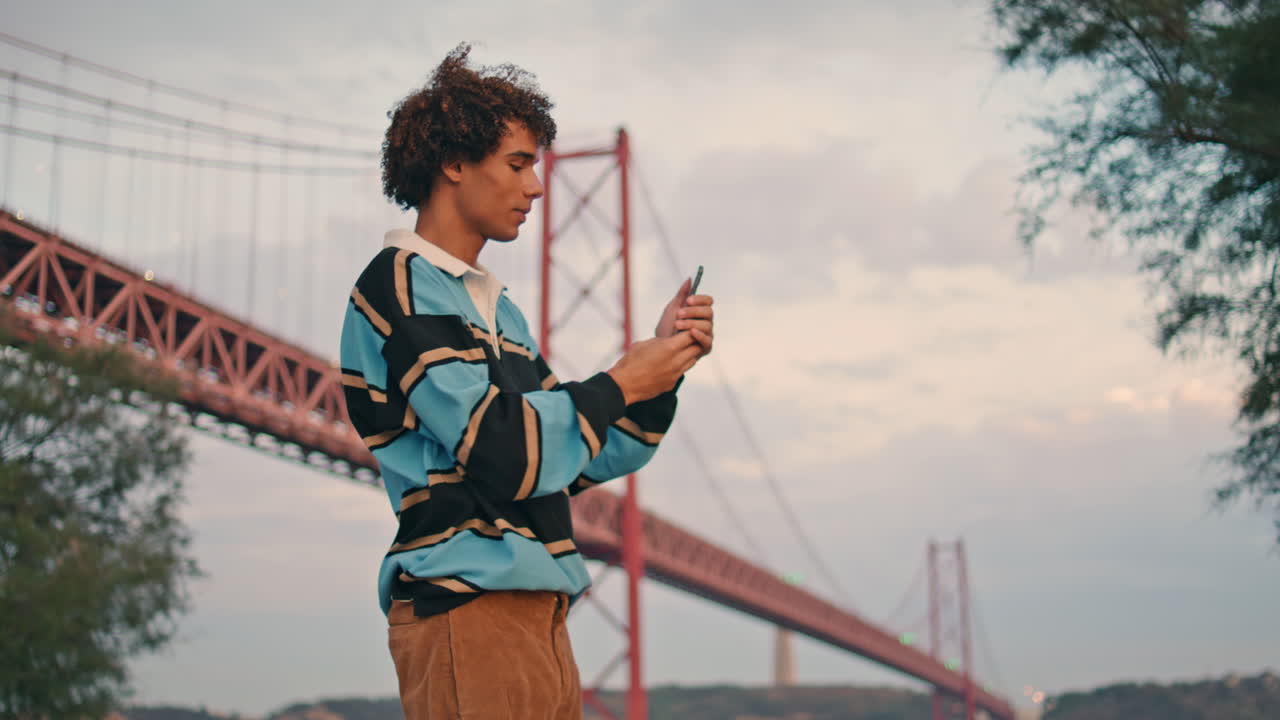 Curly traveler making photos smartphone evening. Positive student with mobile