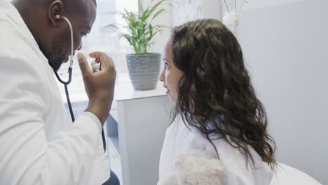 Happy-diverse-doctor-examining-sick-girl-patient-with-stethoscope-in-hospital-in-slow-motion