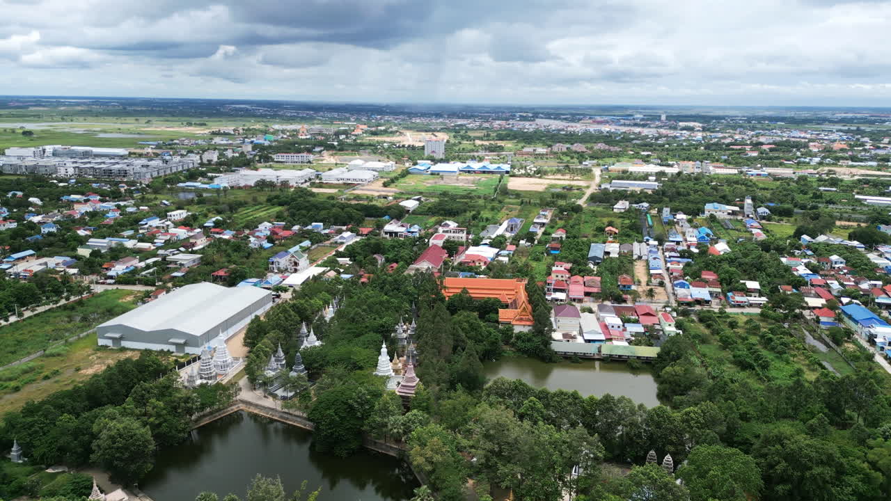 Aerial video of Phnom Penh captures scattered rooftops, farmland, and a temple complex surrounded by trees