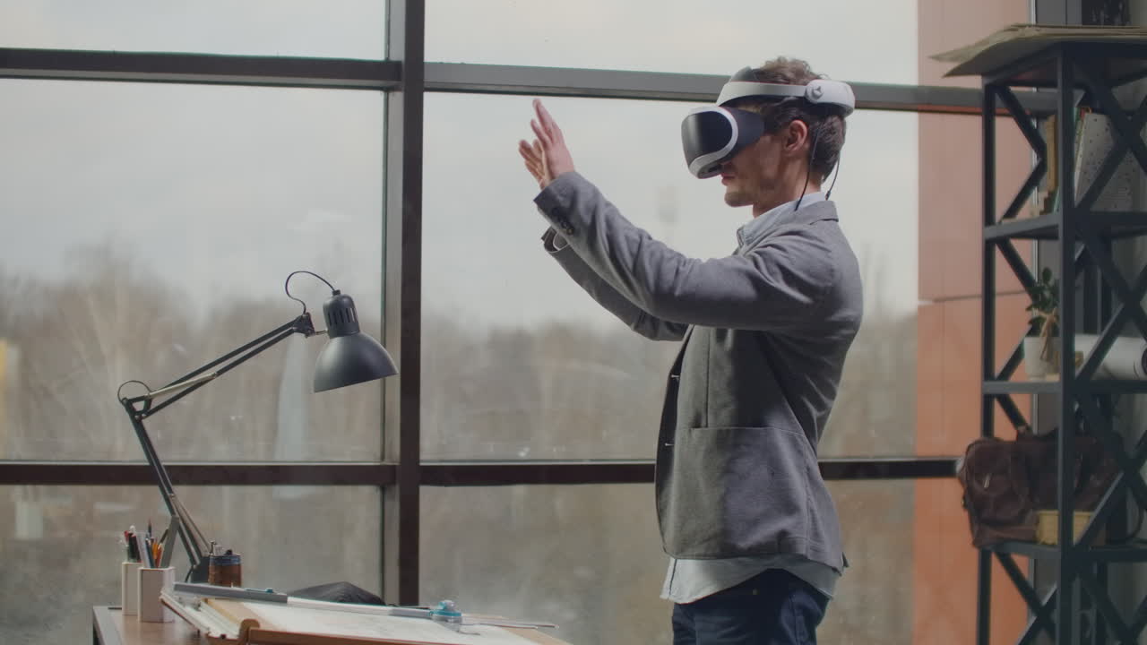 male engineer in a virtual reality helmet near the large window with his hands imitates the work of the interface. Designing the future the concept of virtual architecture and design interface graphic applications.