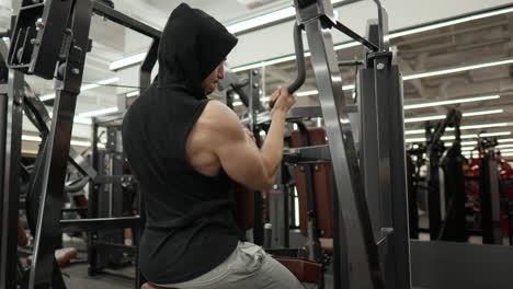 muscular man training back doing one hand lat pulldown exercise in machine at modern gym