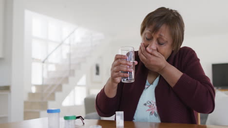 mujer mayor afroamericana tomando pastillas de medicación y agua potable