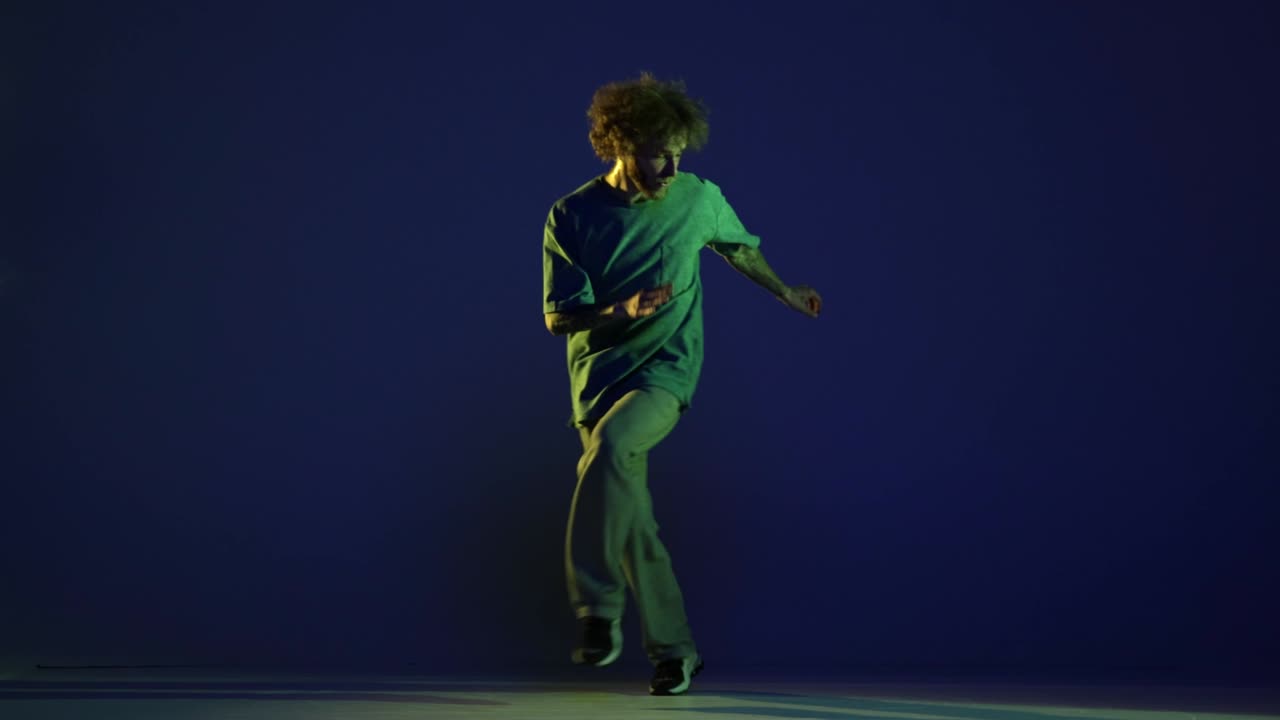 Stylish young man, hip-hop dancer dancing isolated over dark blue background in neon light. Modern dance art, fashion, youth, ad, style. 4K, video