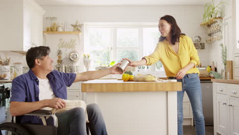 Mature-Asian-couple-with-husband-in-wheelchair-unpacking-fresh-produce-in-kitchen-after-shopping-trip---shot-in-slow-motion