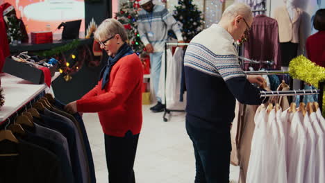 Ältere-Frau-Und-Ehemann-Stöbern-Durch-Kleiderständer-In-Einem-Weihnachtlich-Geschmückten-Bekleidungsgeschäft.-Älteres-Ehepaar-Freut-Sich,-Nachdem-Es-Perfekte-Blazer-Gefunden-Hat,-Die-Es-Seinem-Enkel-Schenken-Kann