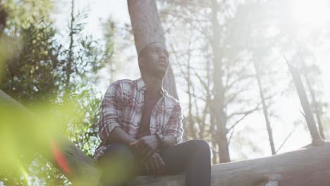 smiling african american man sitting on tree during hiking in countryside