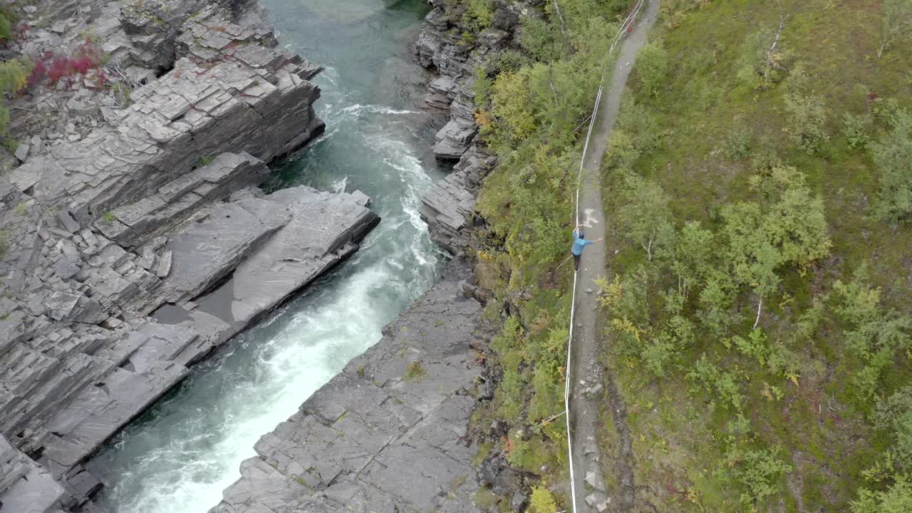 un hombre que camina a lo largo de un pasamanos junto a un camino y un río que fluye rápido - durante el día
