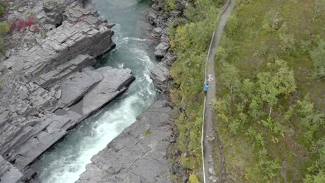 A-man-walking-along-a-hand-rail-next-to-a-pathway-and-fast-flowing-river---Daytime