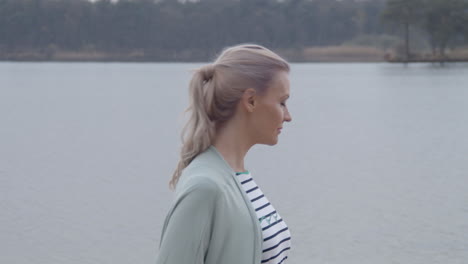 beautiful woman standing near lakeside and turning towards camera