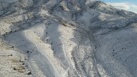 4K-aerial-scenic-view-of-drone-slowly-pulling-back-and-revealing-snowy-mountains,-Tempiute-mountain-with-clouds-and-patches-of-blue-sky-in-the-late-afternoon