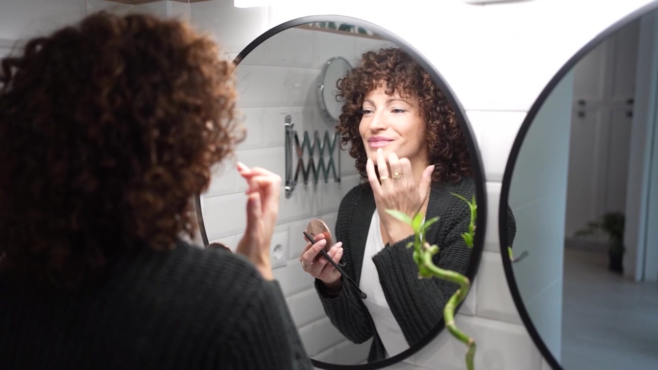 Una donna si trucca guardando il suo riflesso in un elegante specchio da bagno