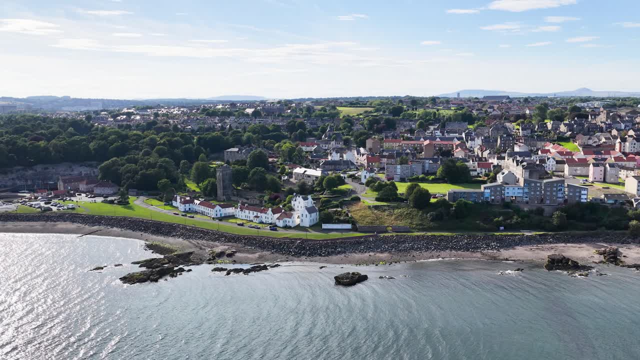 Drone glides above seaside town, revealing shoreline, historic buildings, and bright summer lighting