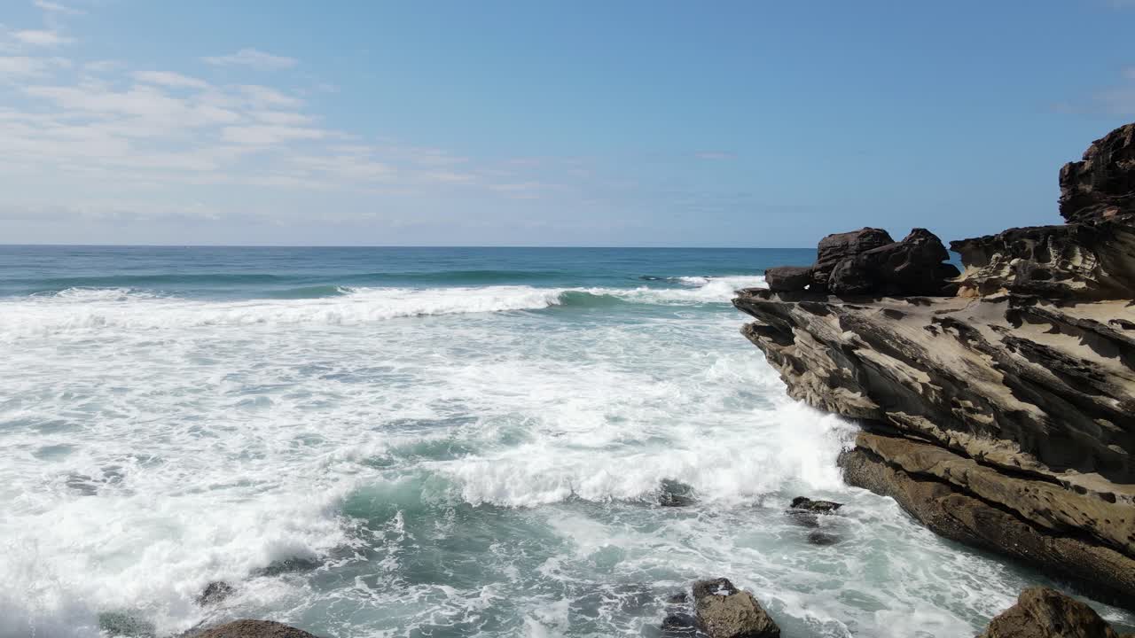emergiendo lentamente de una cala rocosa oculta con olas que chocan contra el escarpado promontorio costero