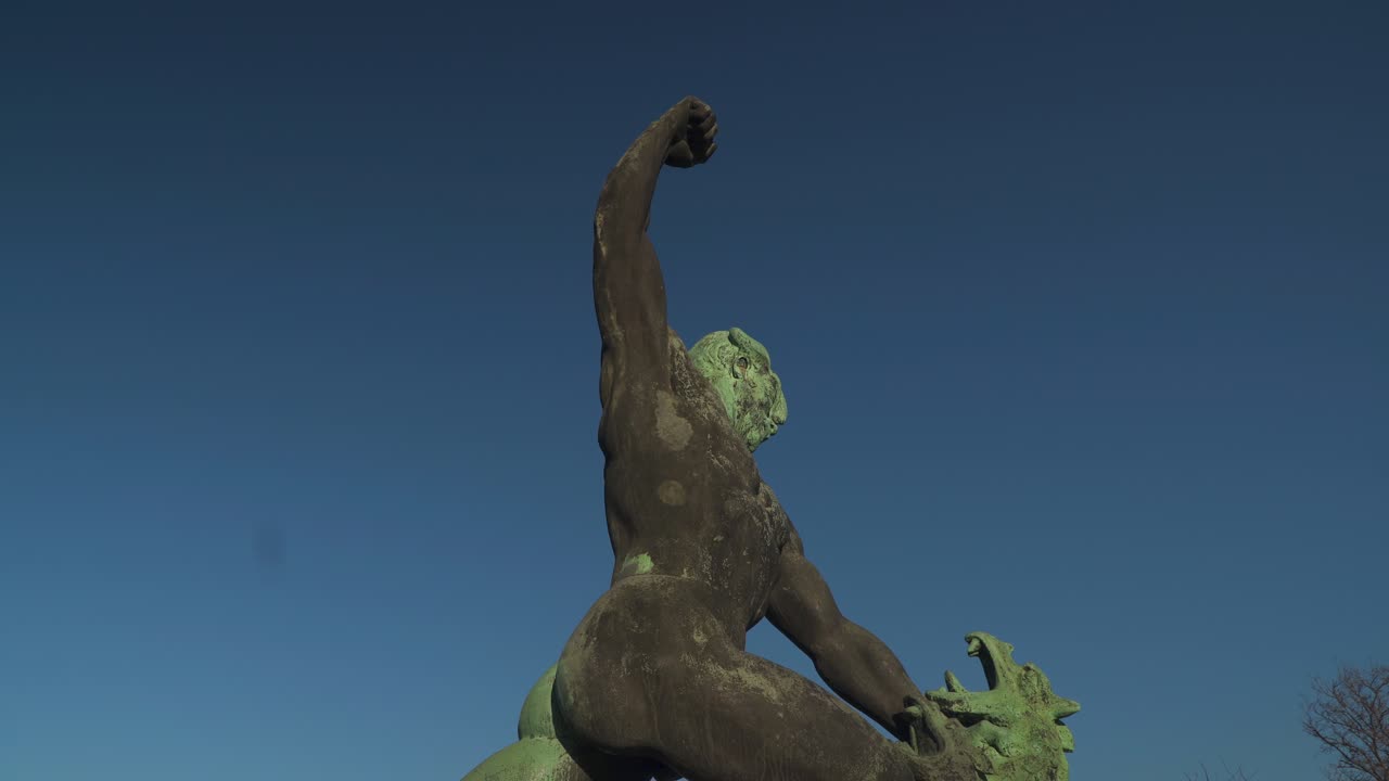 Statue of a Hungarian warrior fighting a three-headed dragon In Budapest, Hungary With Blue Sky - Tilt Down Shot