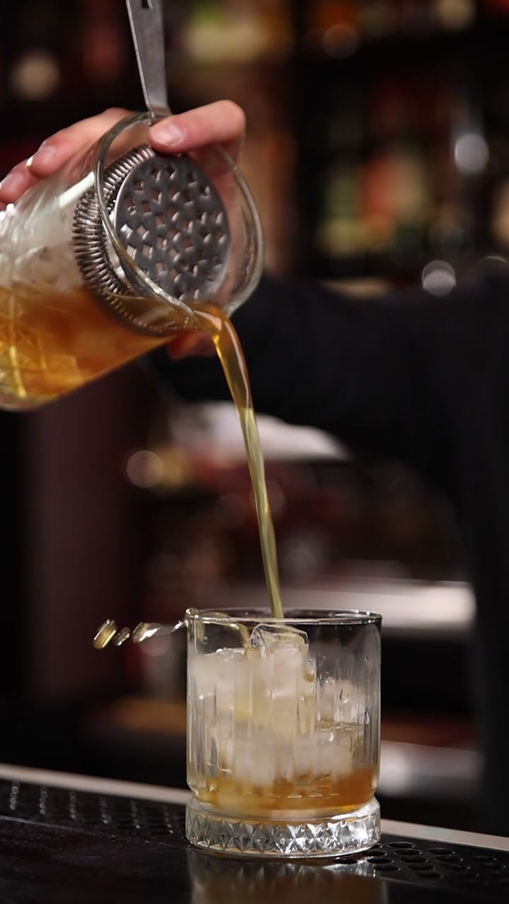 Barman che versa un cocktail ambrato in un bicchiere con ghiaccio