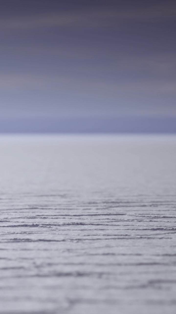 Calm water reflects sky colors during twilight near the shoreline