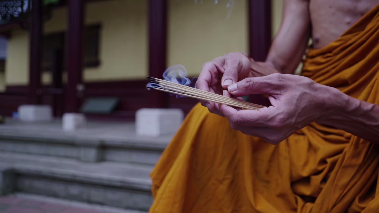 Close-up video angle of a monk's hands holding incense sticks, with smoke swirling