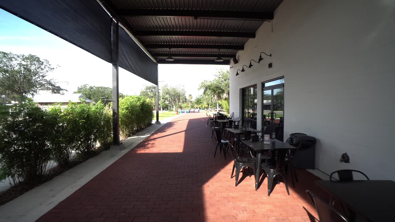 Avvicinamento grandangolare sotto una tenda da sole che copre i posti a sedere all'aperto di un tavolo e sedie da caffè in metallo.