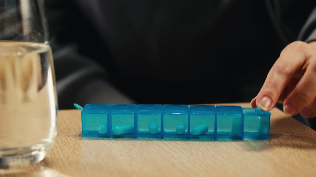 persona que toma medicamentos diarios con un organizador de pastillas y un vaso de agua
