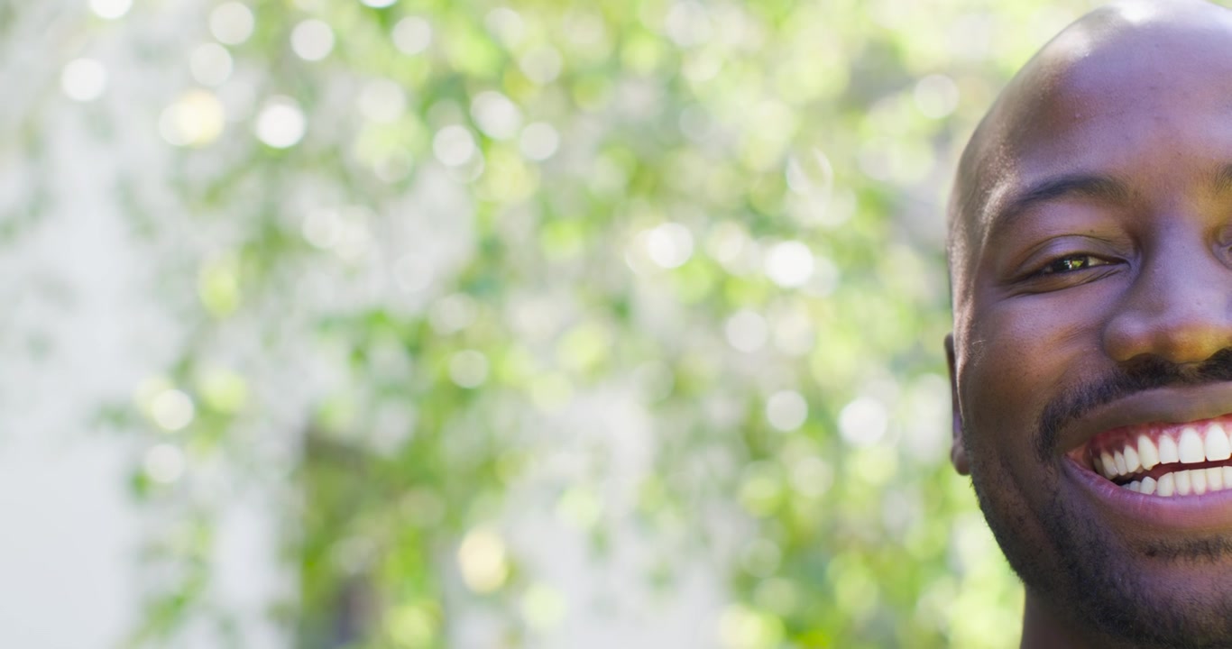 African man hearing offscreen joke, smiling and laughing outdoors with bokeh foliage, copy space